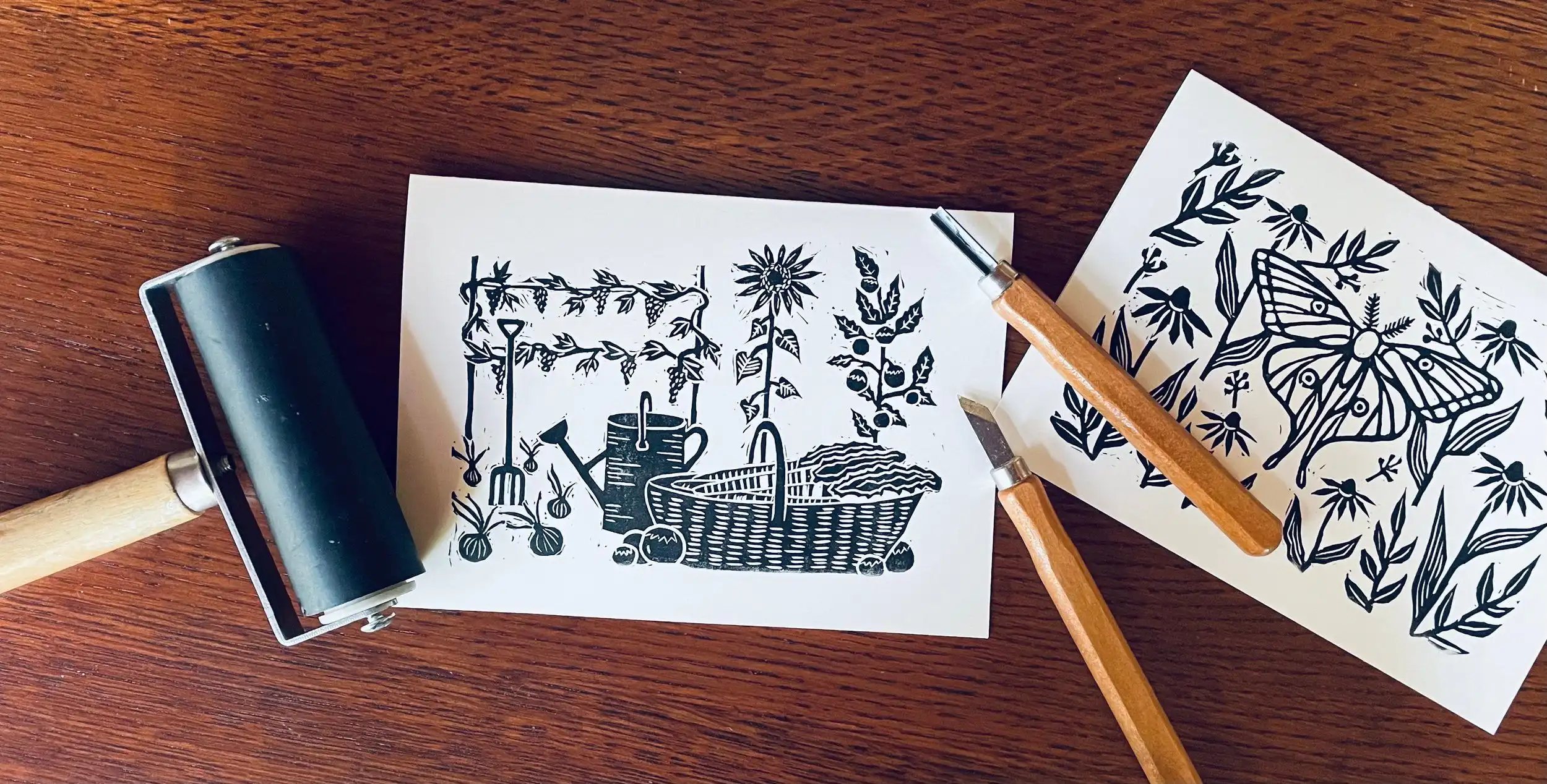 A brayer, carving tools and two freshly pulled greeting cards on a wooden table